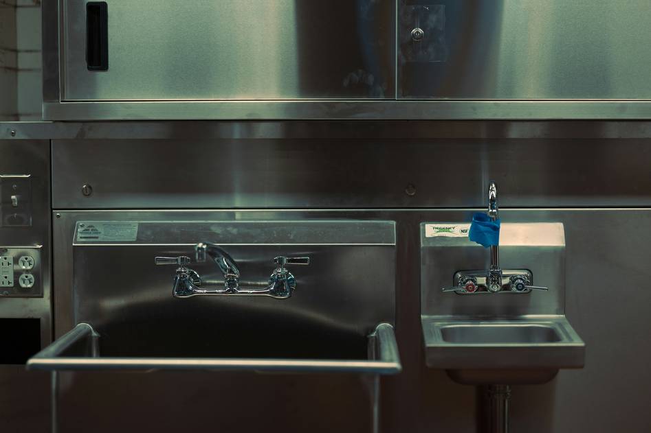 Hands holding a brushed stainless steel coffee mug on a wooden kitchen counter with morning light